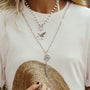 Person wearing a necklace with floral and bird pendants, holding a straw hat.-4